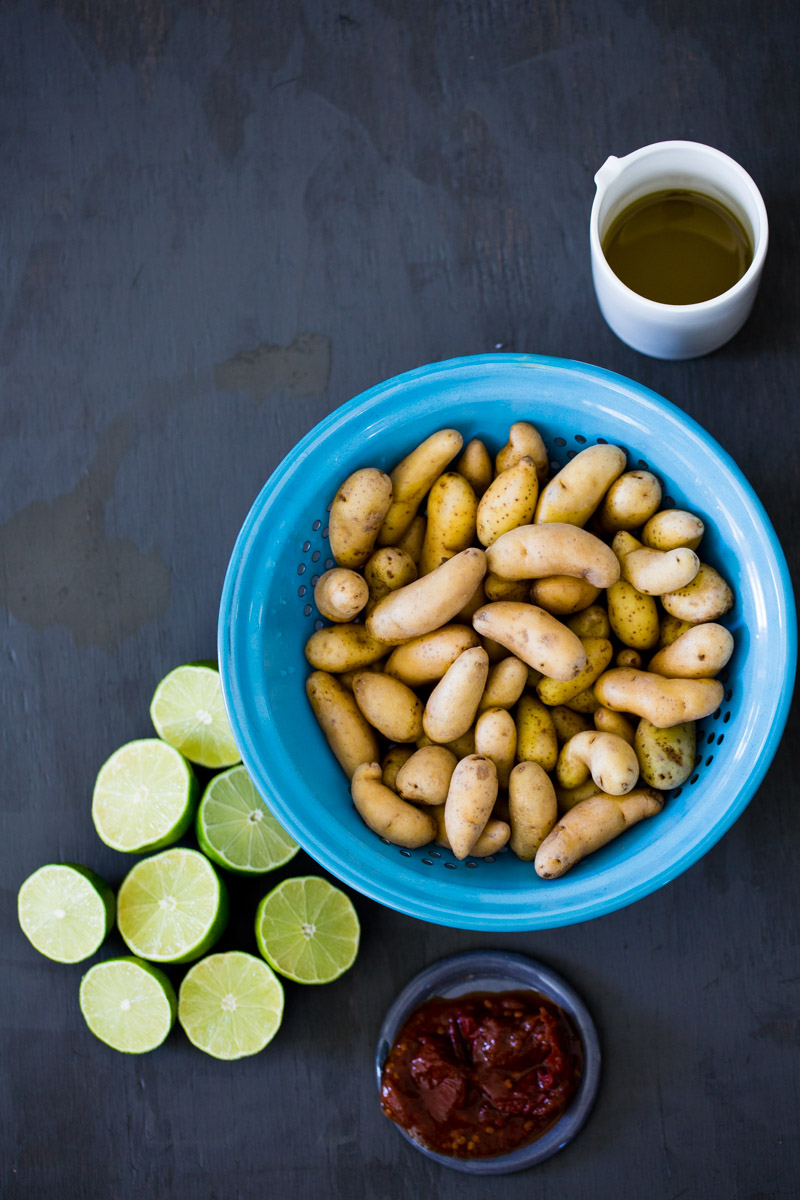 Papas en colador, limones partidos a la mitad, aceite de oliva en vaso blanco