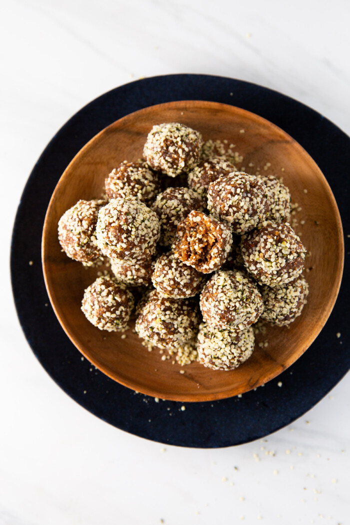 Bolitas de almendra y dátil cubiertas con semillas de hemp. Están sobre un plato de madera.