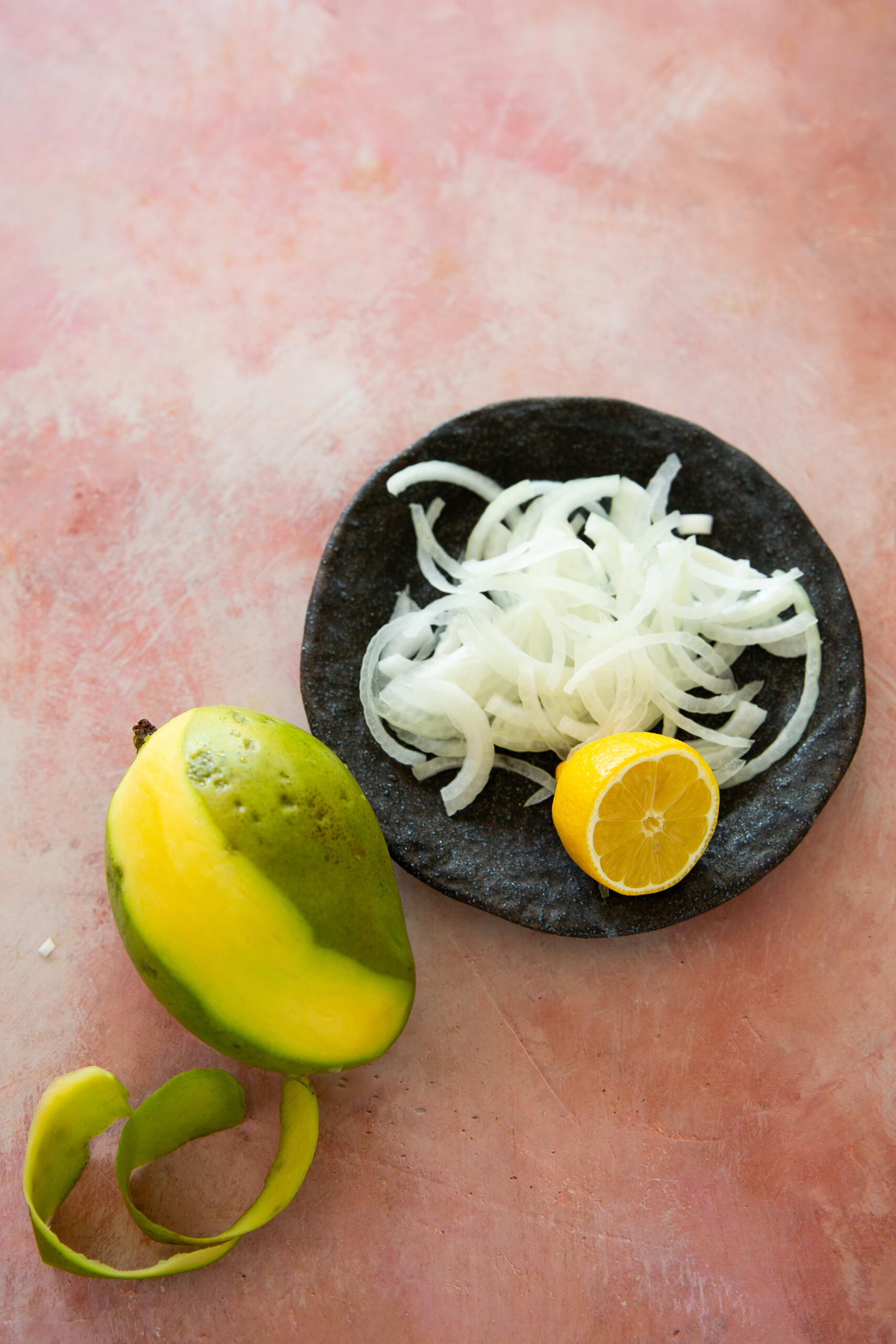 Ingredientes para ensalada de mango verde: cebolla rebanada, limón y un mango medio pelado sobre una tabla.
