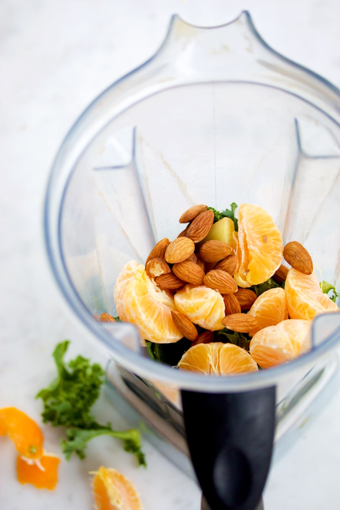 Mandarina, kale y almendras para hacer smoothie verde en el vaso de la licuadora.