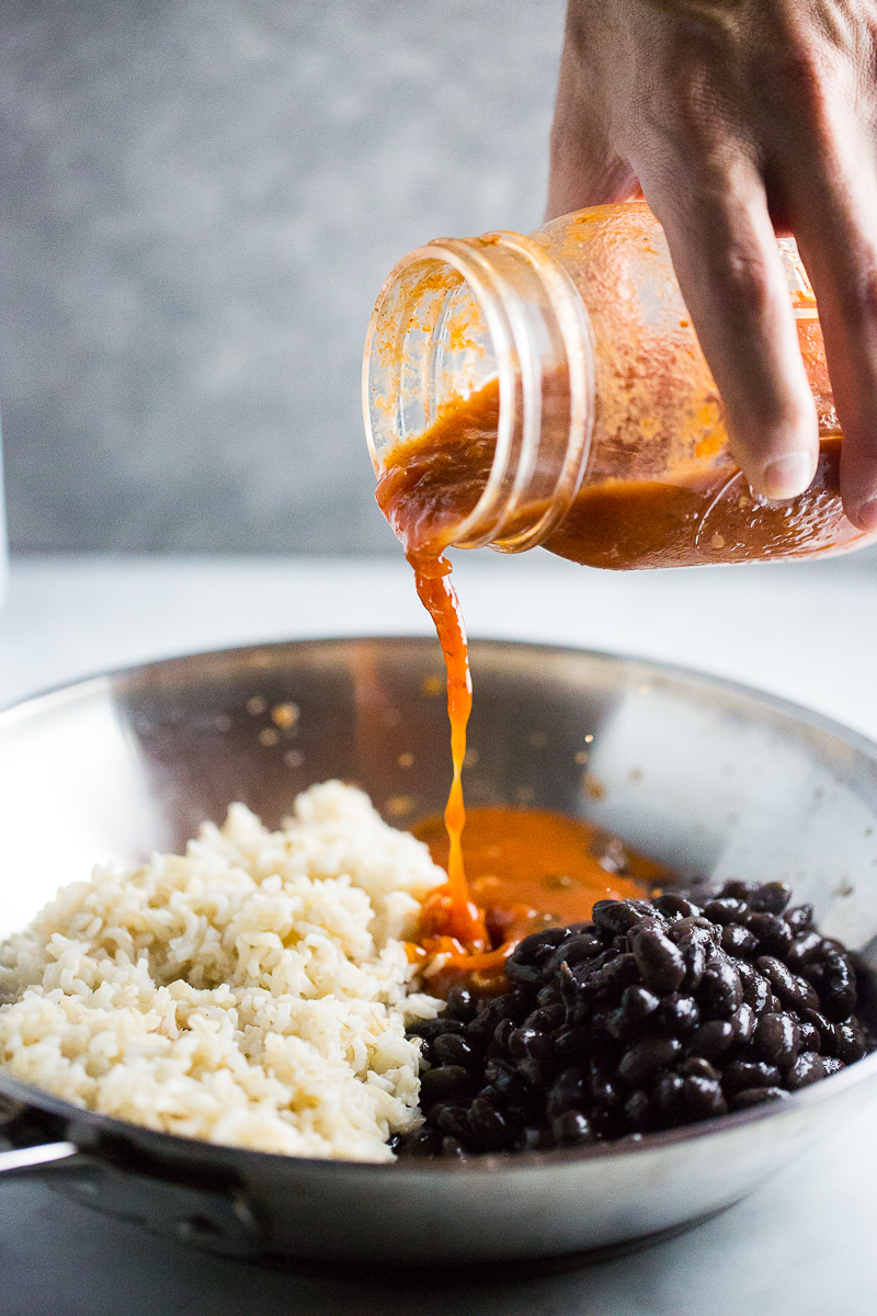 Sirviendo salsa de enchilada a un sartén con arroz y frijol.