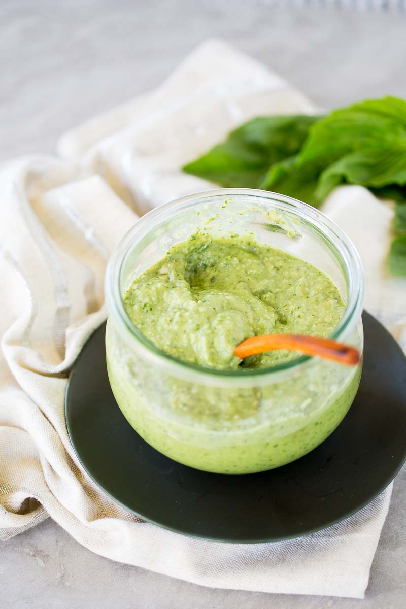 Pesto de aguacate para todo un frasco de vidrio sobre un plato negro.