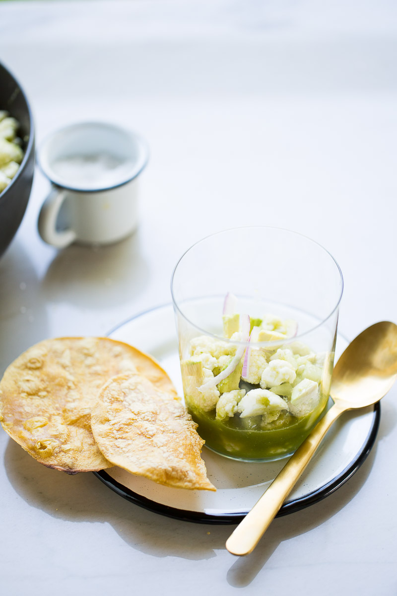 Aguachile de coliflor servido en un vaso y tostadas de maíz aun lado.