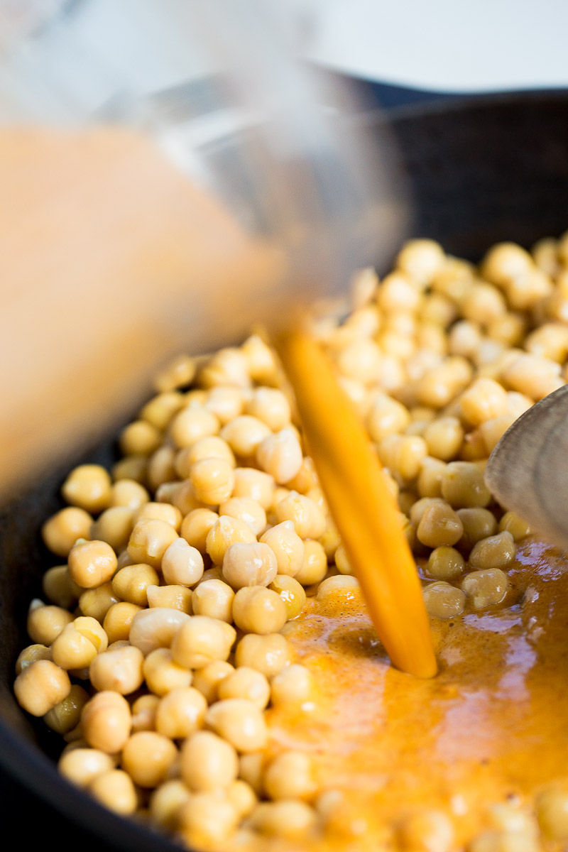 vaciando el mole coloradito al sartén con garbanzos