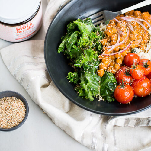 The Mexican Buddha bowl is a bowl with rice, sautéed green leaves, roasted vegetables and chickpeas in a creamy sauce of Oaxacan mole Coloradito.