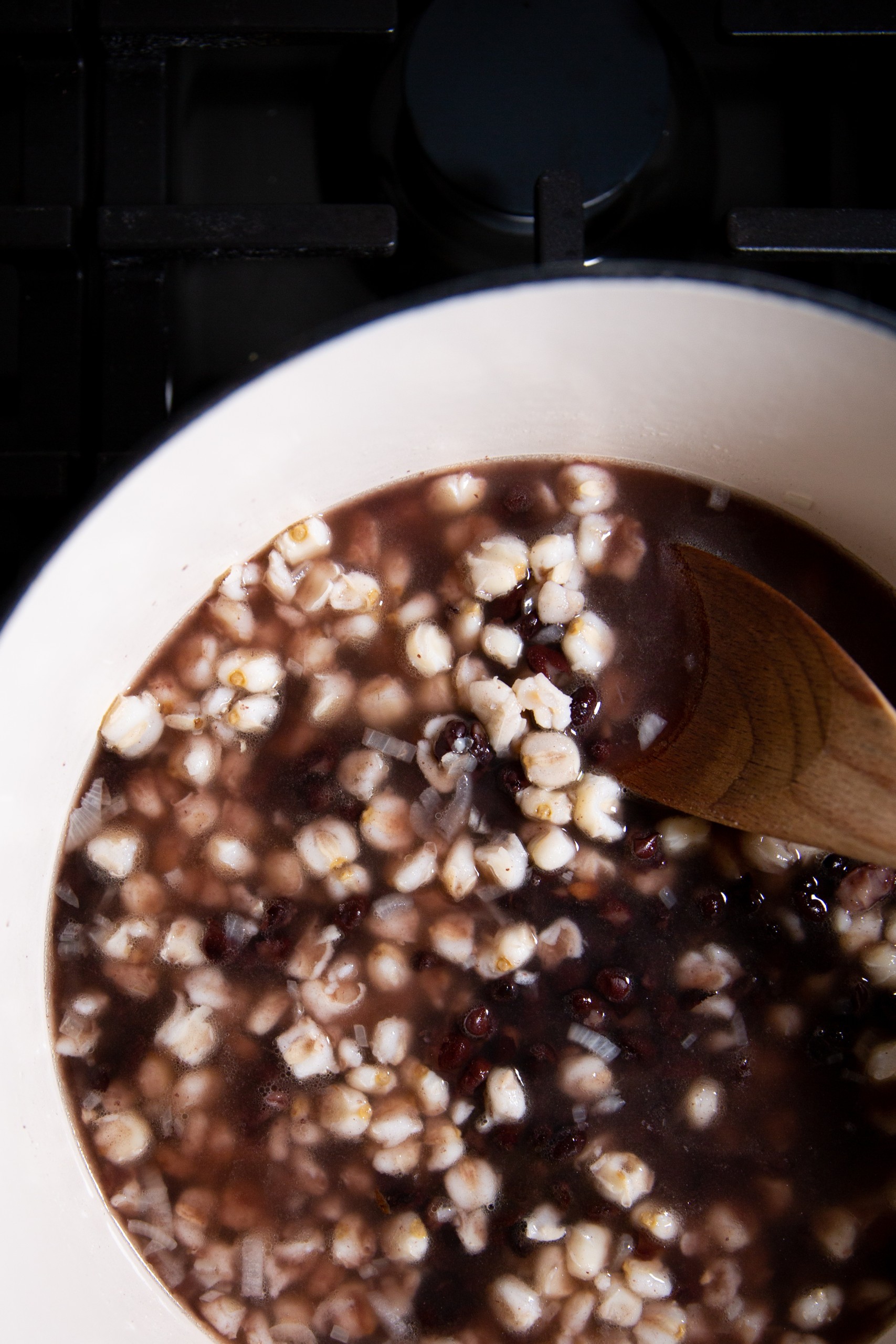 Un taz&oacute;n humeante de pozole con frijol negro con toppings frescos y una cuchara de madera