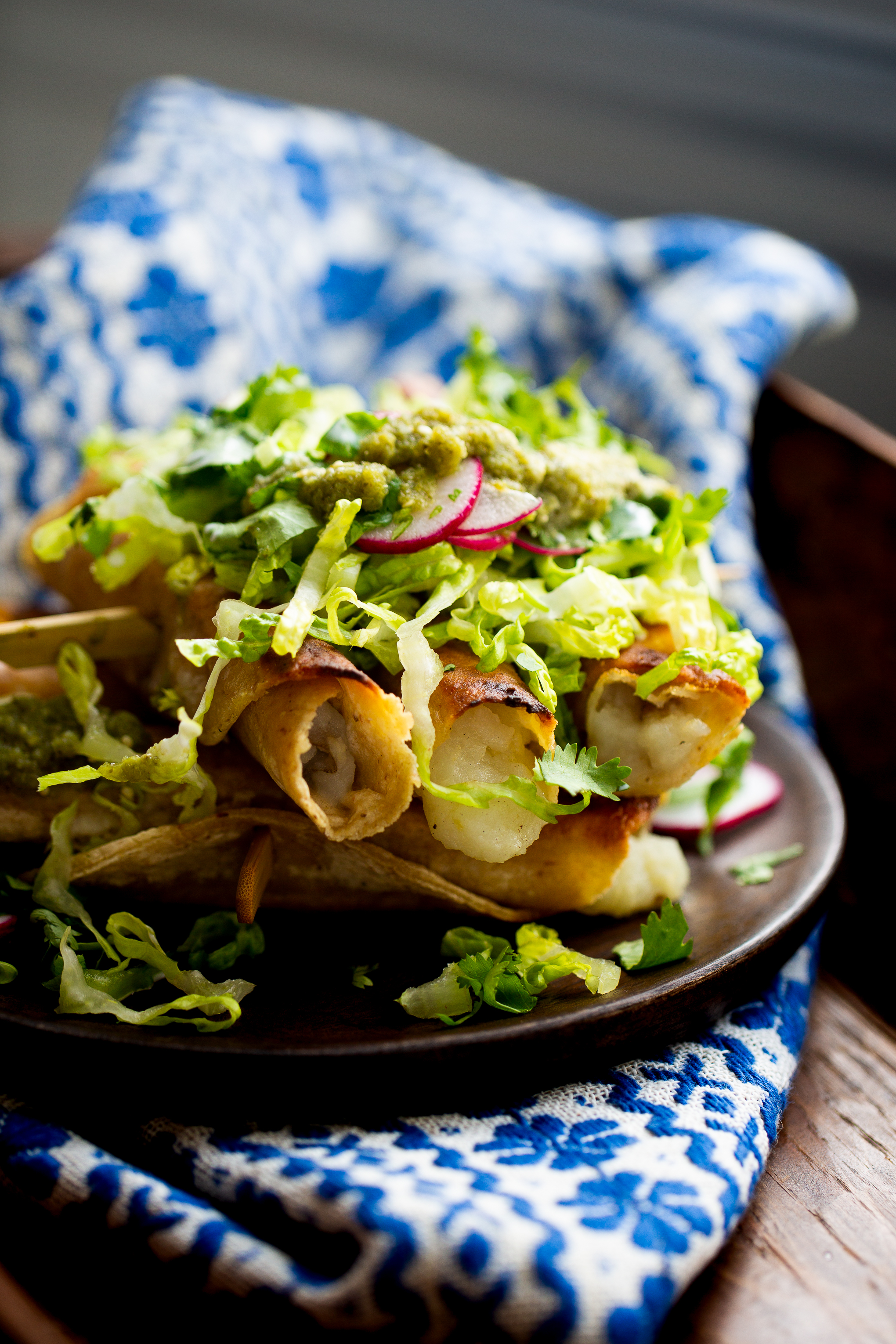 Flautas mexicanas de papa con lechuga, salsa, crema y rábanos.