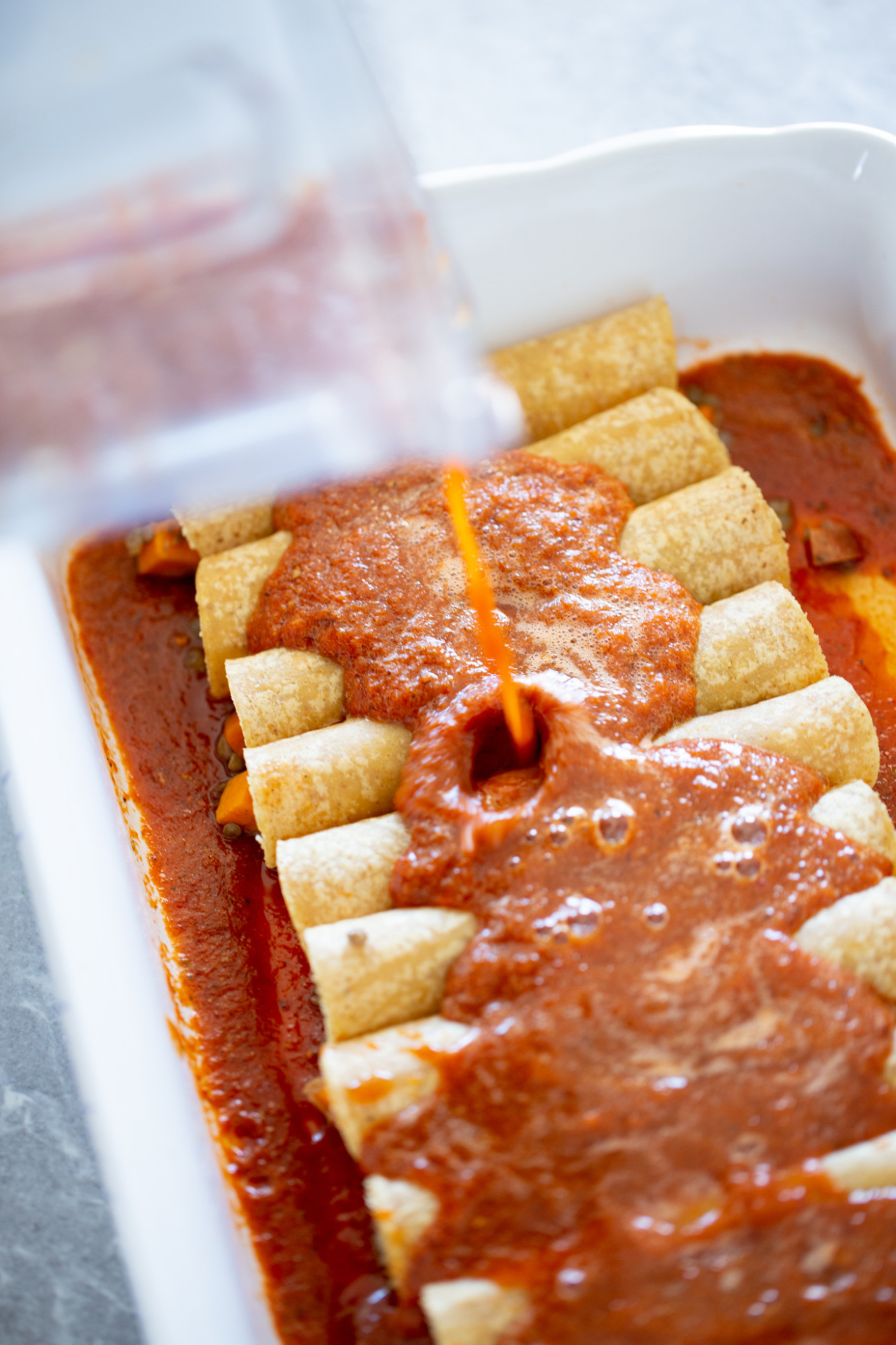 Sirviendo salsa roja con chile ancho sobre tortillas rellenas tipo enchilada