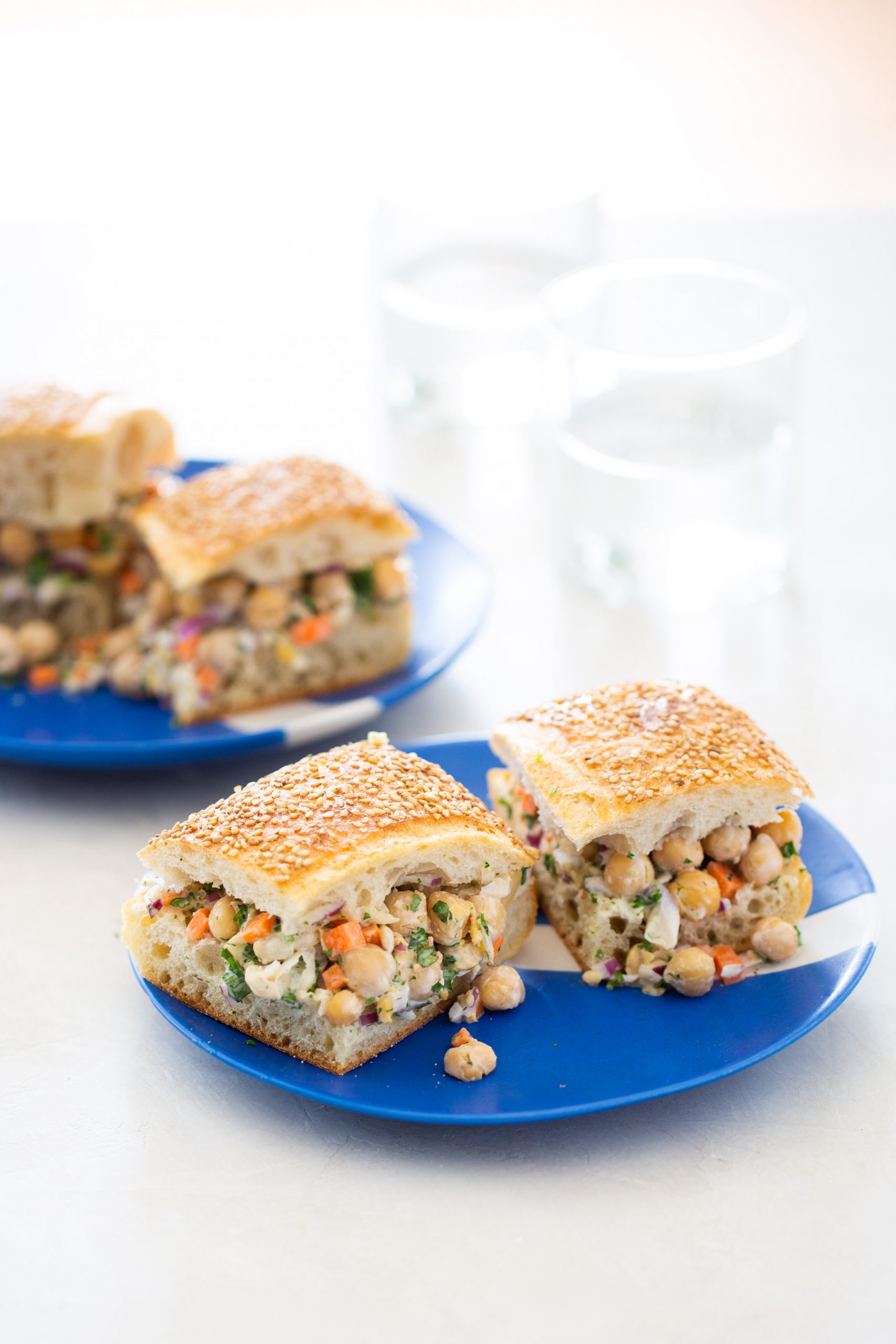 Sándwiches de ensalada de garbanzo en un plato azul con vasos de agua al fondo.