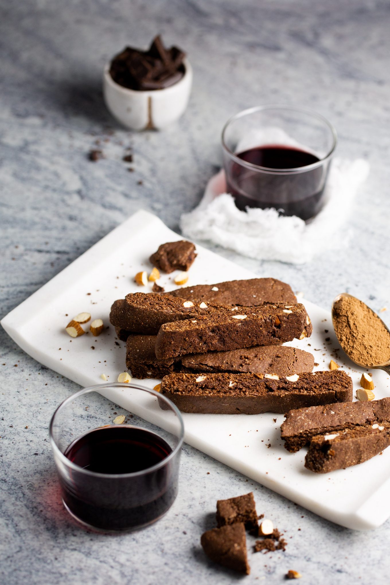 Biscotti de chocolate sobre una charola blanca y un vaso con vino tinto.