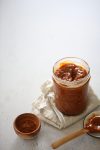 Un frasco de salsa de caramelo al lado de una cuchara de madera, con chamoy.