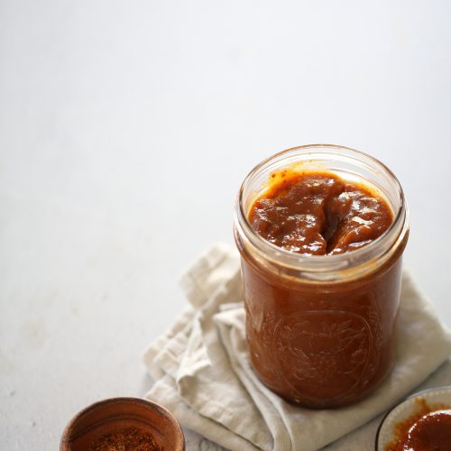 Un frasco de salsa de caramelo al lado de una cuchara de madera, con chamoy.