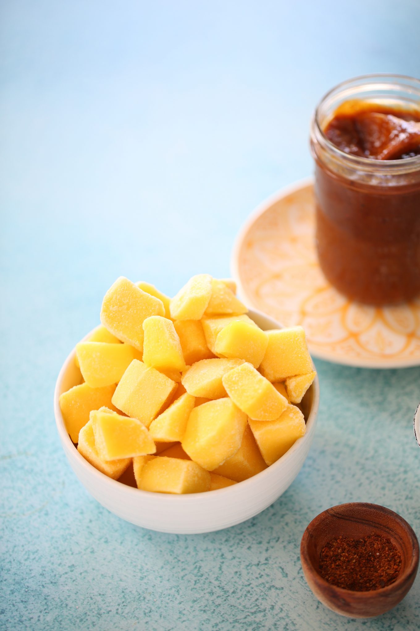 un tazón con mango congelado y un frasco de chamoy hecho en casa