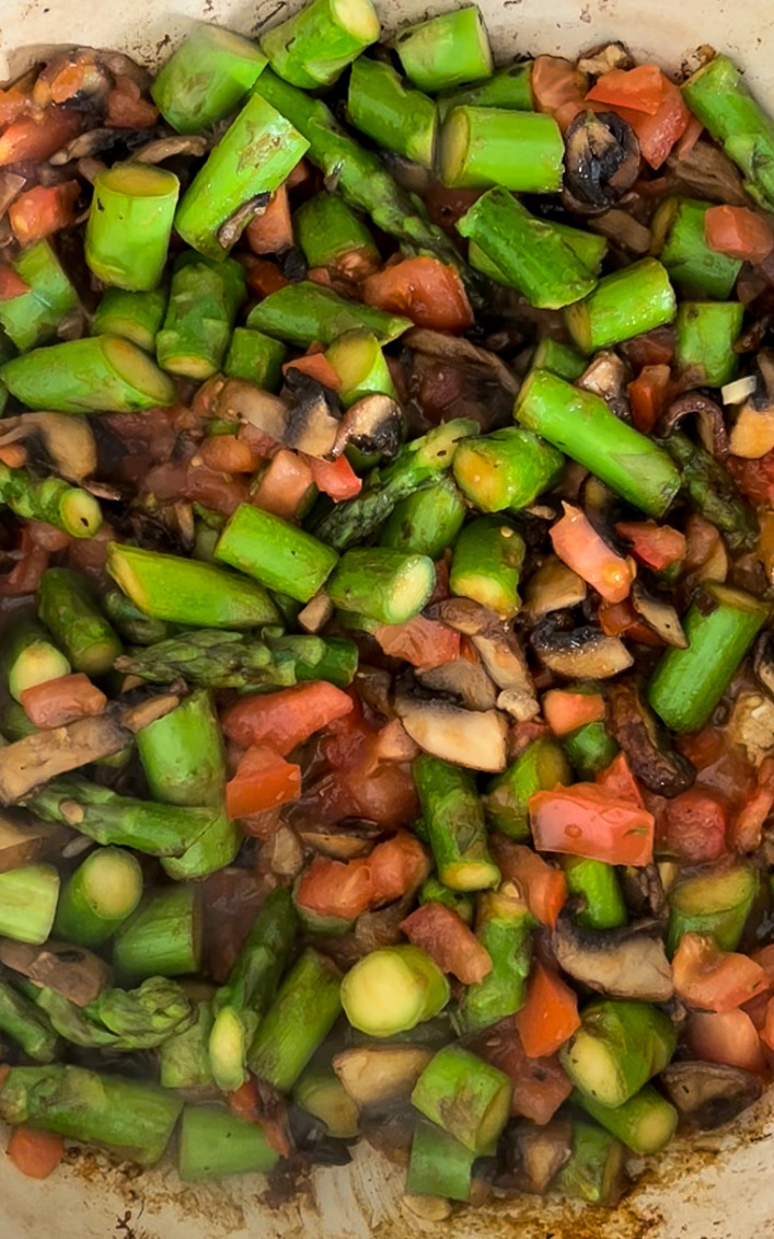 Esp&aacute;rragos, champi&ntilde;ones y tomate picado cocin&aacute;ndose en un sart&eacute;n