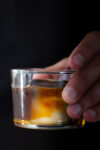 A person holding a glass with ice and carajillo in it.