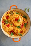 Pasta con tomates cherry y albahaca en una olla naranja.