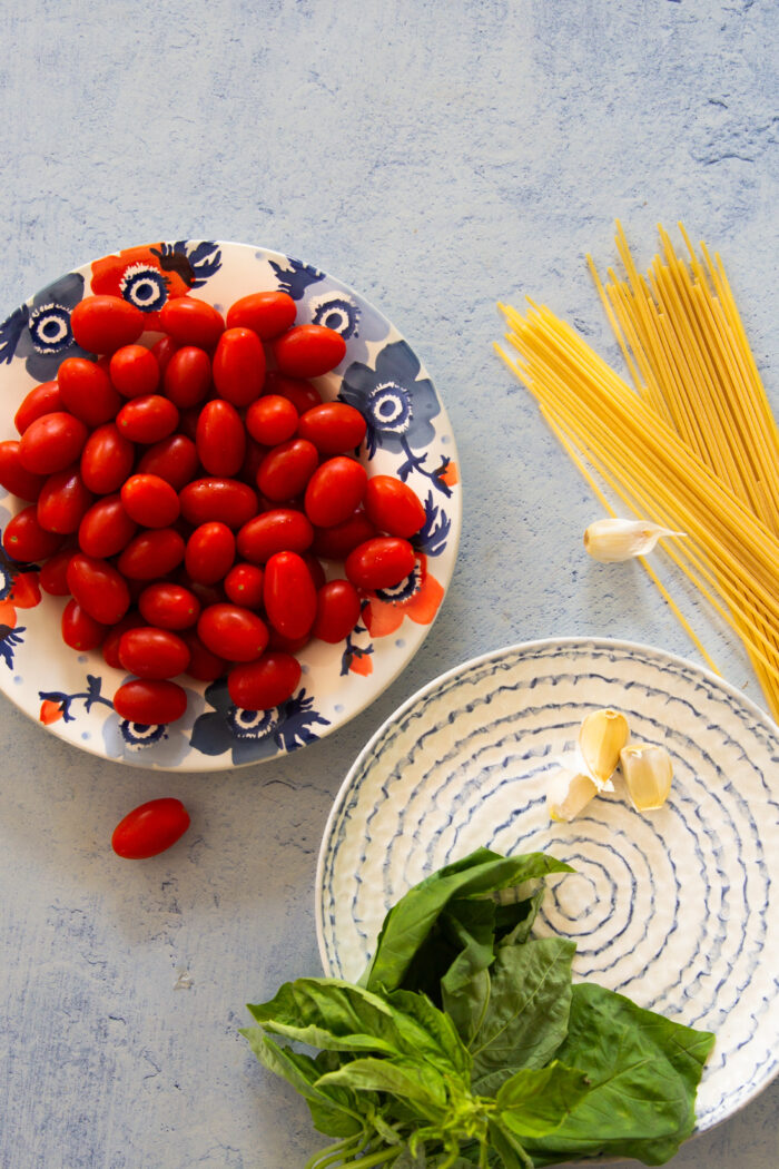 un platao con tomatitos, hojas de albahaca fresca, espagueti seco y dientes de ajo