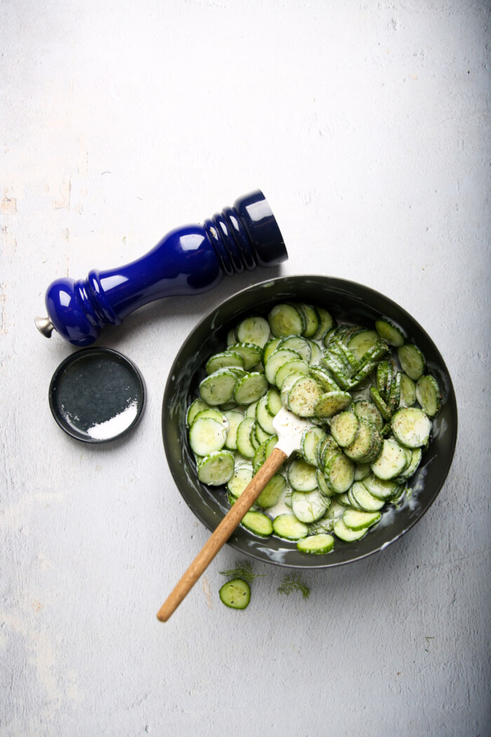 cucumber dill salad in a bowl with salt dish  and pepper on the side.