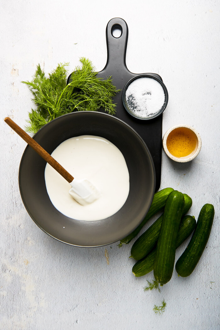 A bowl with yogurt, cucumbers and apple cider and dill on the side