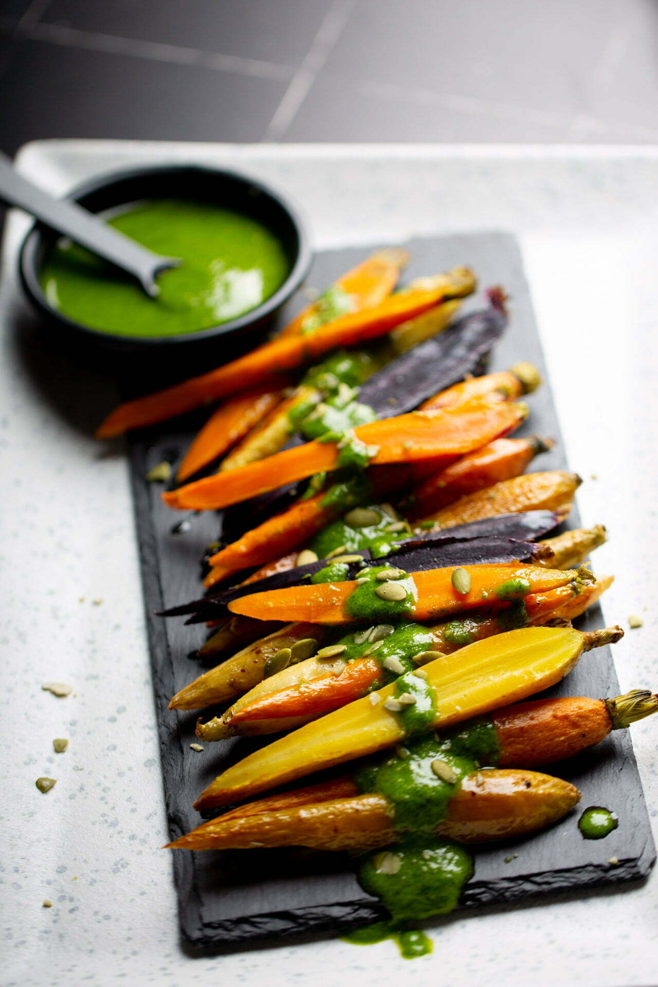 Roasted carrots with a green sauce on a slate plate.