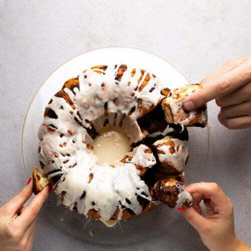 Two hands holding a vegan bundt cake on a plate.