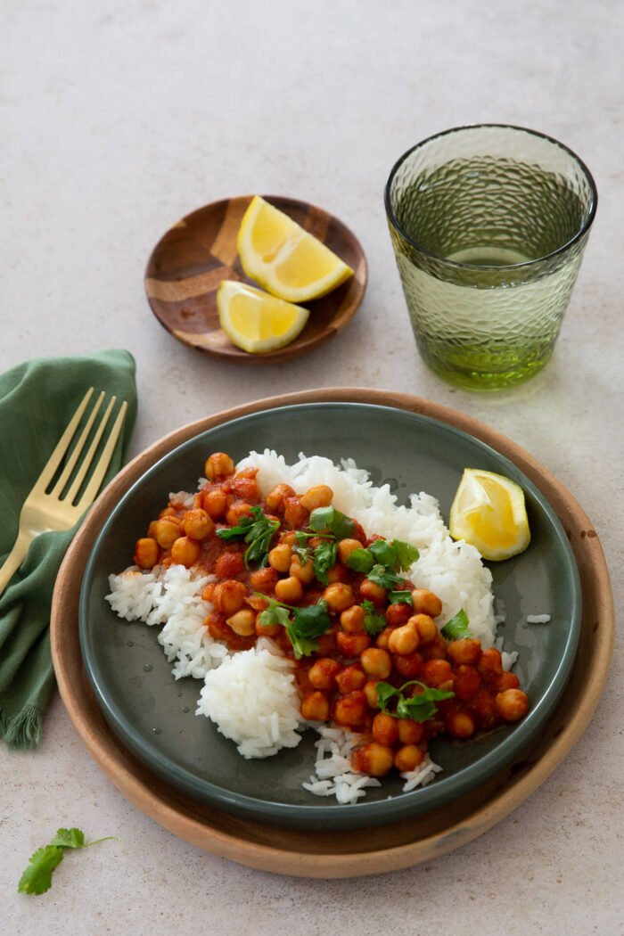 Chana masala sobre arroz blanco con cilantro encima y un limon amarillo a un lado.