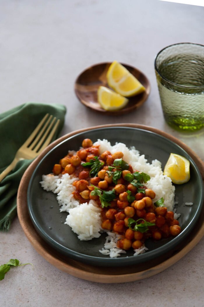 Chana masala sobre arroz blanco en un plato verde fuerte.