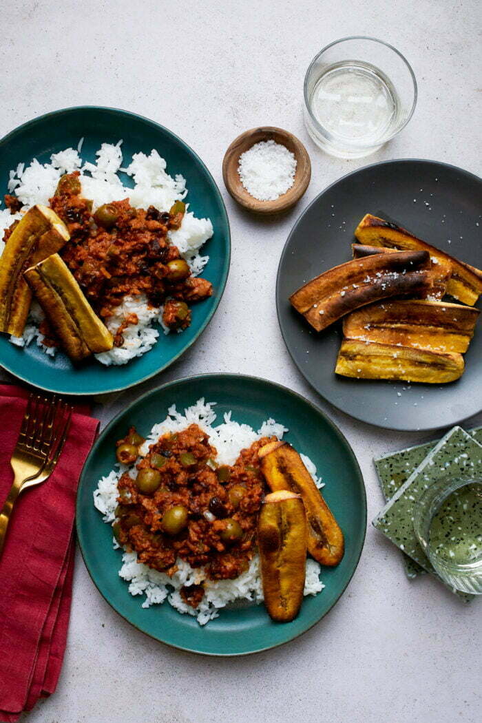 Dos platos con arroz blanco cubierto con picadillo cubano y plátanos.