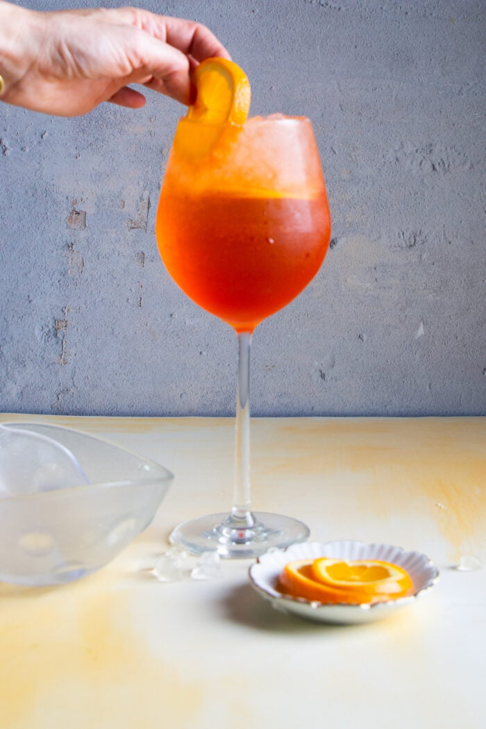 Poniendo una rebanada de naranja a una copa con aperol spritz 