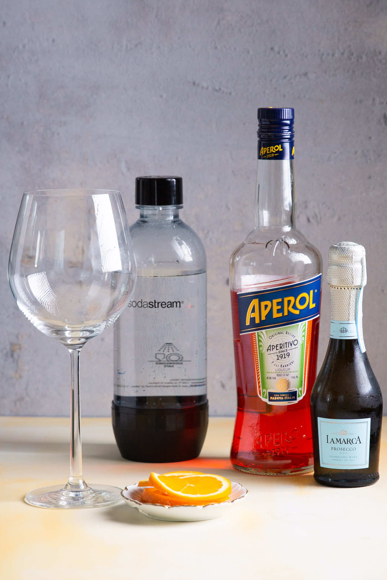 Copa de vino vac&iacute;a, botella de soda, botella de Aperol y botella de Prosecco