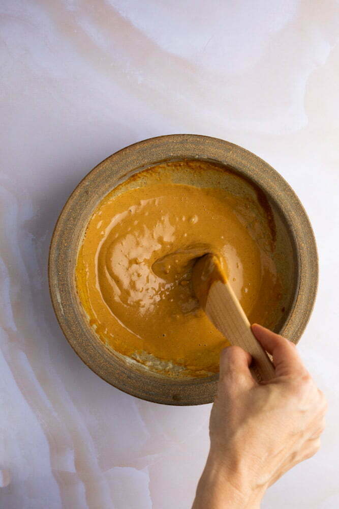 Salsa de cacahuate cremosa en un taz&oacute;n con cuchara de madera.