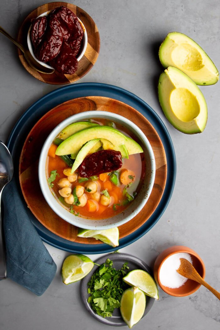 caldo tlalpeno vegano en un plato con cilantro y limones a un lado