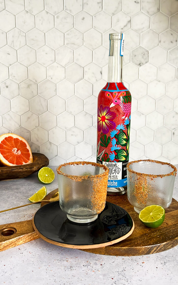 botella de mezcal, vasos escarchados y limones y tornjas