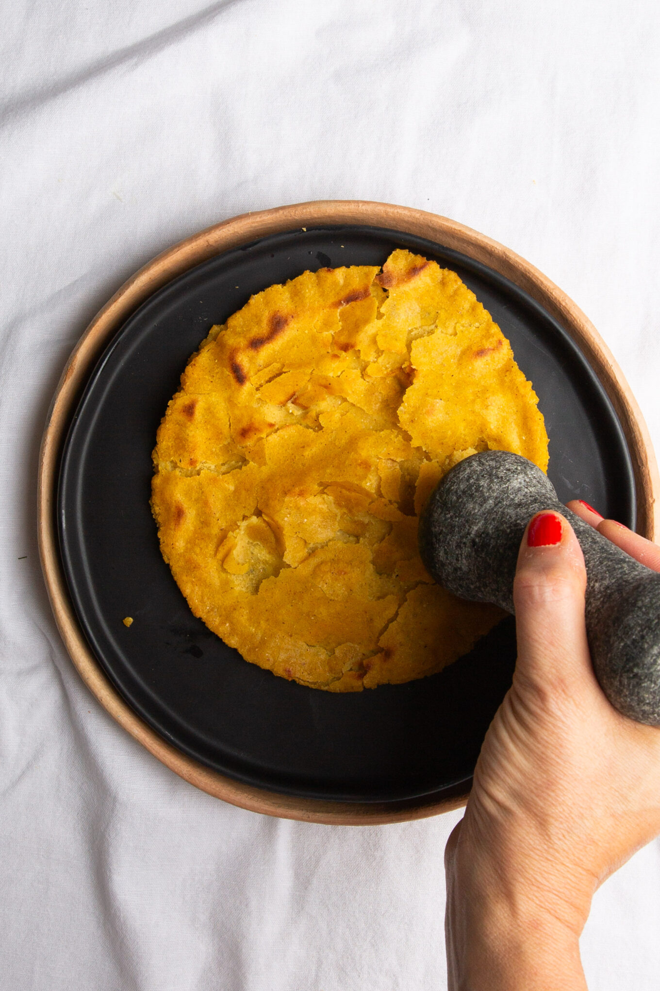 Una persona usando una piedra para aplanar una tortilla al estilo tradicional veracruzana.