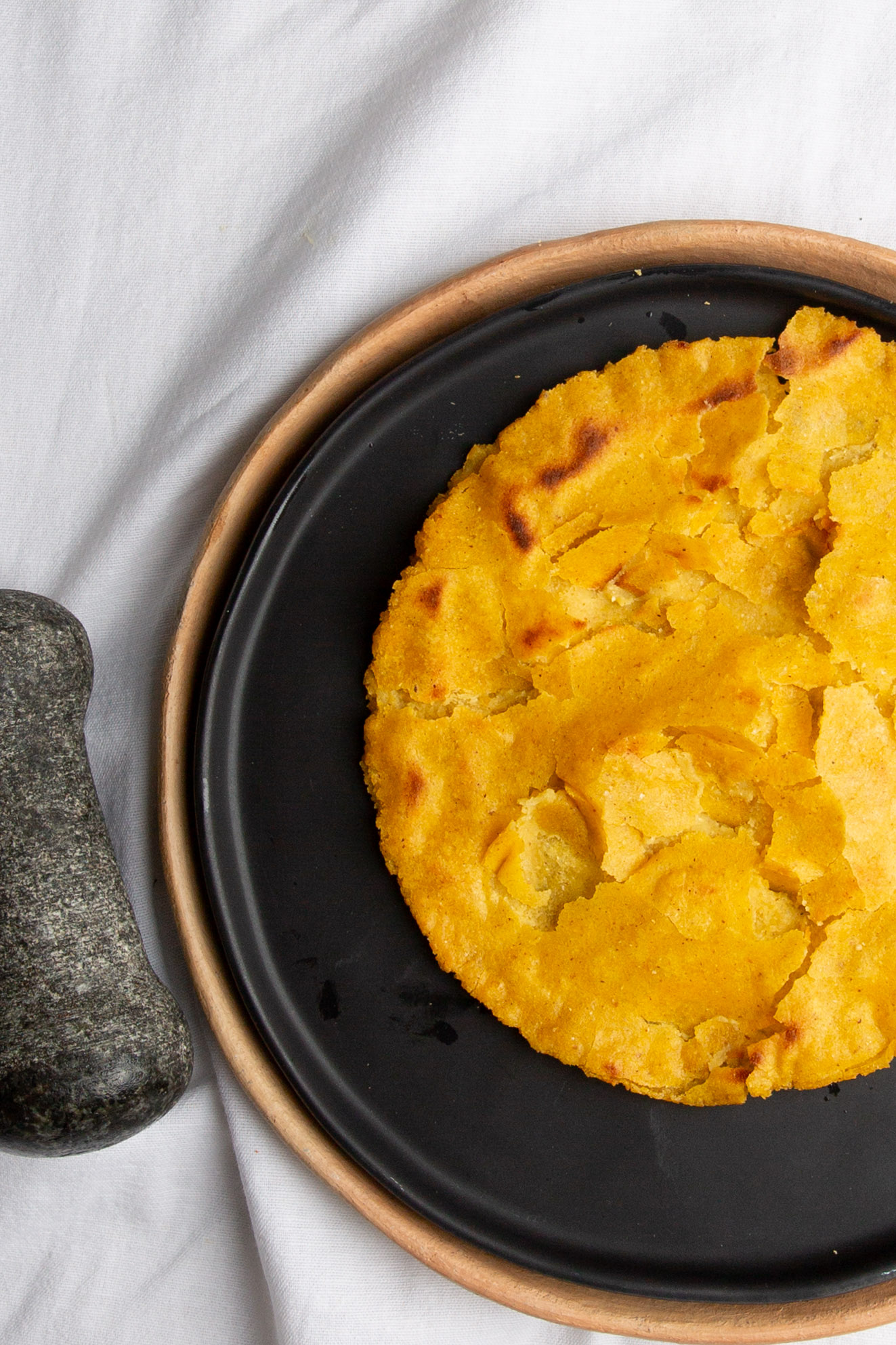Una tortilla sobre un plato negro junto a una piedra, inspirada en las veracruzanas.