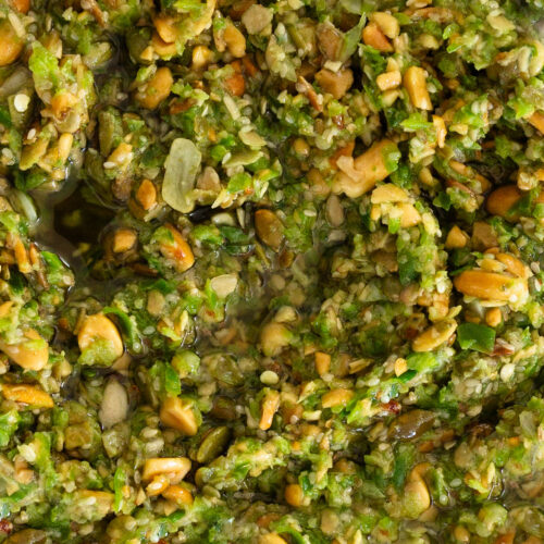 Primer plano de un cuenco de pesto verde con pipas de calabaza.