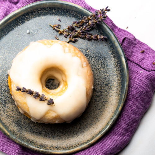 Un donut vegano de tarta de limón con glaseado de lavanda en un plato.