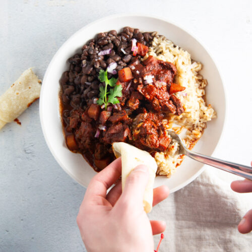 Una persona comiendo un plato de frijoles negros y arroz.