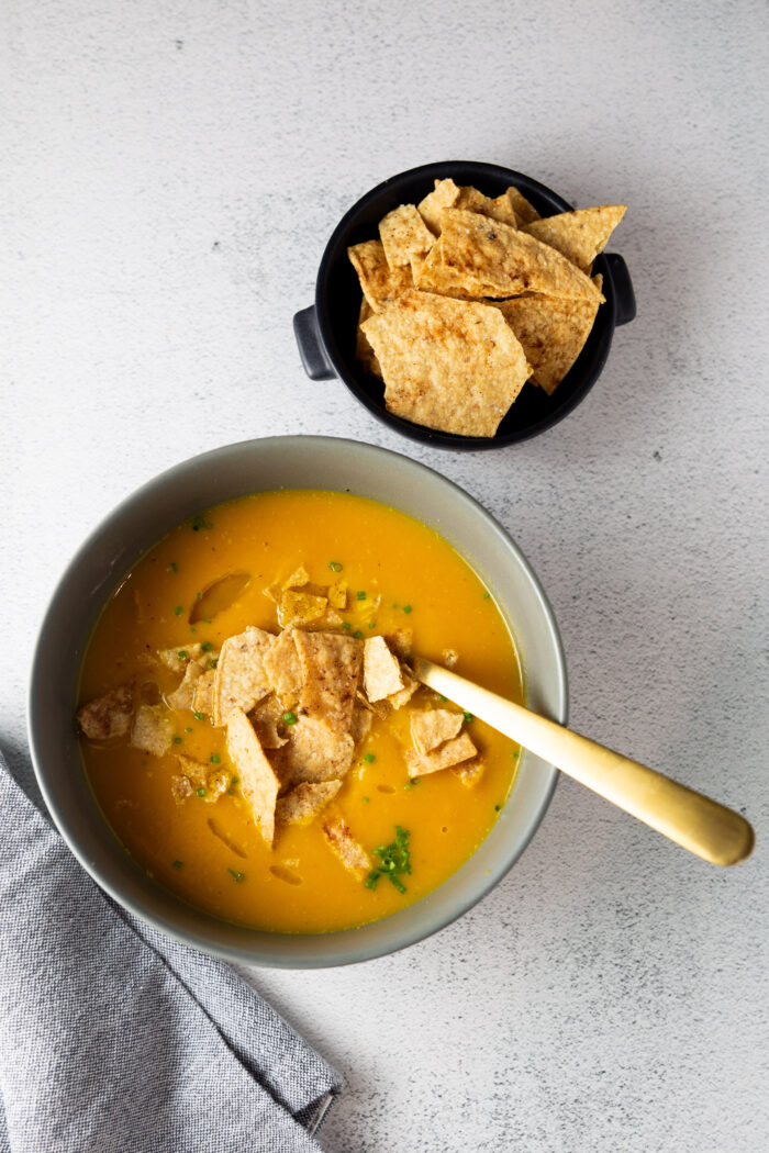 Una receta fácil de sopa de calabaza Butternut con tortilla chips al lado.