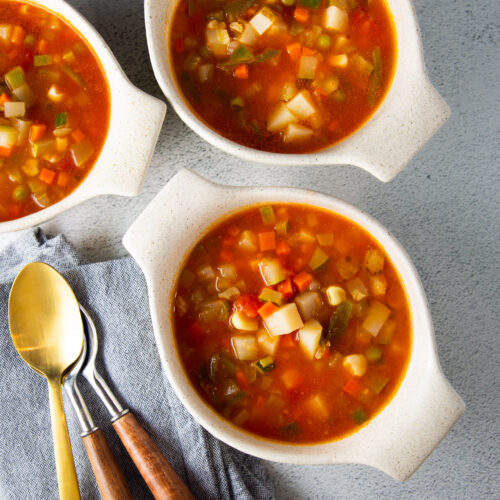 Tres cuencos de sopa de verduras con cucharas en una servilleta.