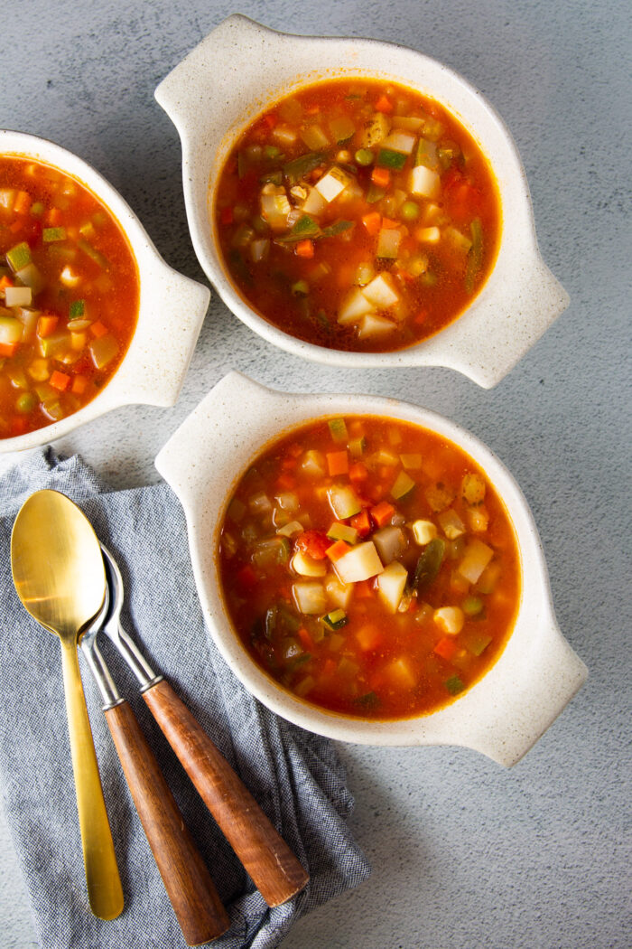 Tres cuencos de sopa de verduras con cucharas en una servilleta.