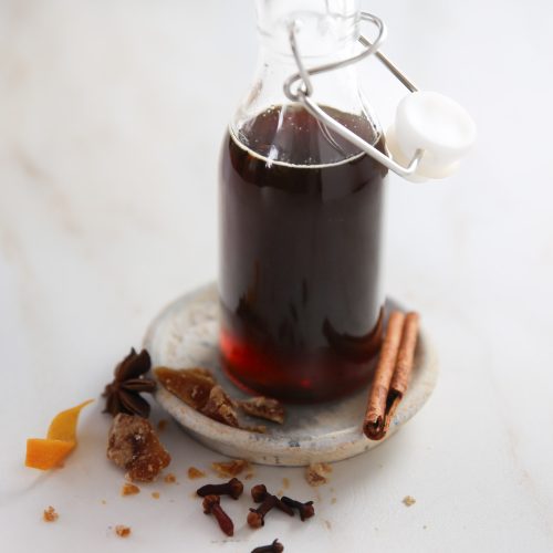 Una botella de vidrio con ramitas de canela y especias en un plato blanco.