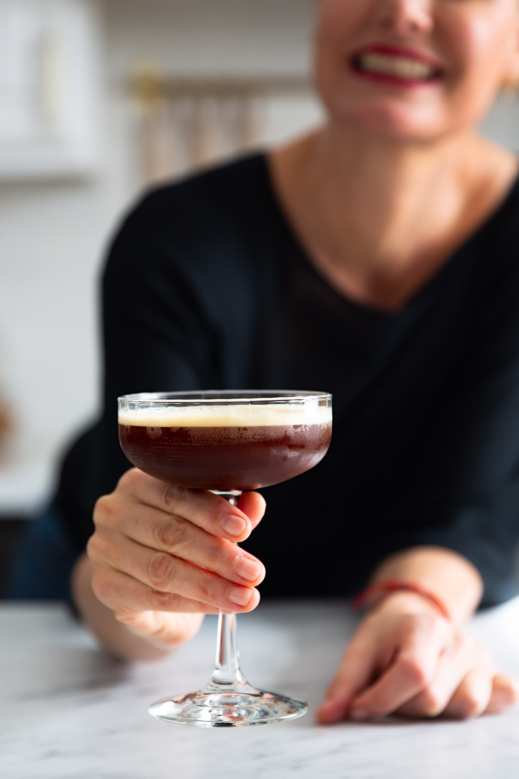 A woman gracefully holding a martini glass, enjoying a Carajillo Shakeado.