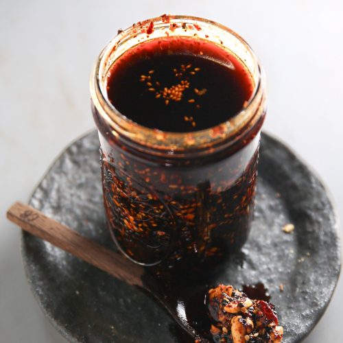 Un bote de salsa macha con una cuchara en un plato.