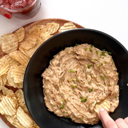 Una persona está mojando un plato de salsa vegana en un plato de salsa.