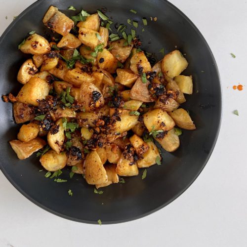 Papas machas en un plato negro con hierbas.