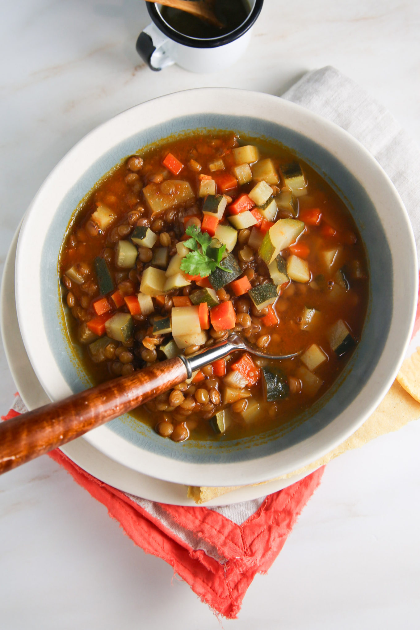 Un plato de sopa de lentejas con verduras y una cuchara.