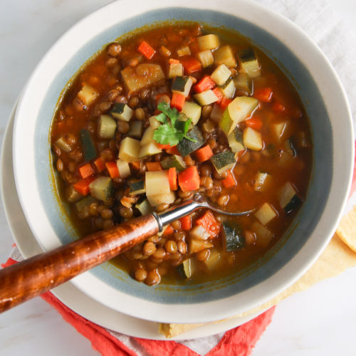 Un plato de sopa de lentejas con verduras y una cuchara.