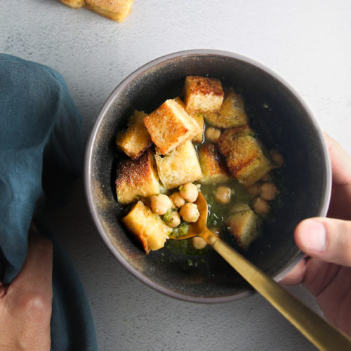 Crutones en un recipiente con una persona sosteniendo una cuchara para Sopa Portuguesa.