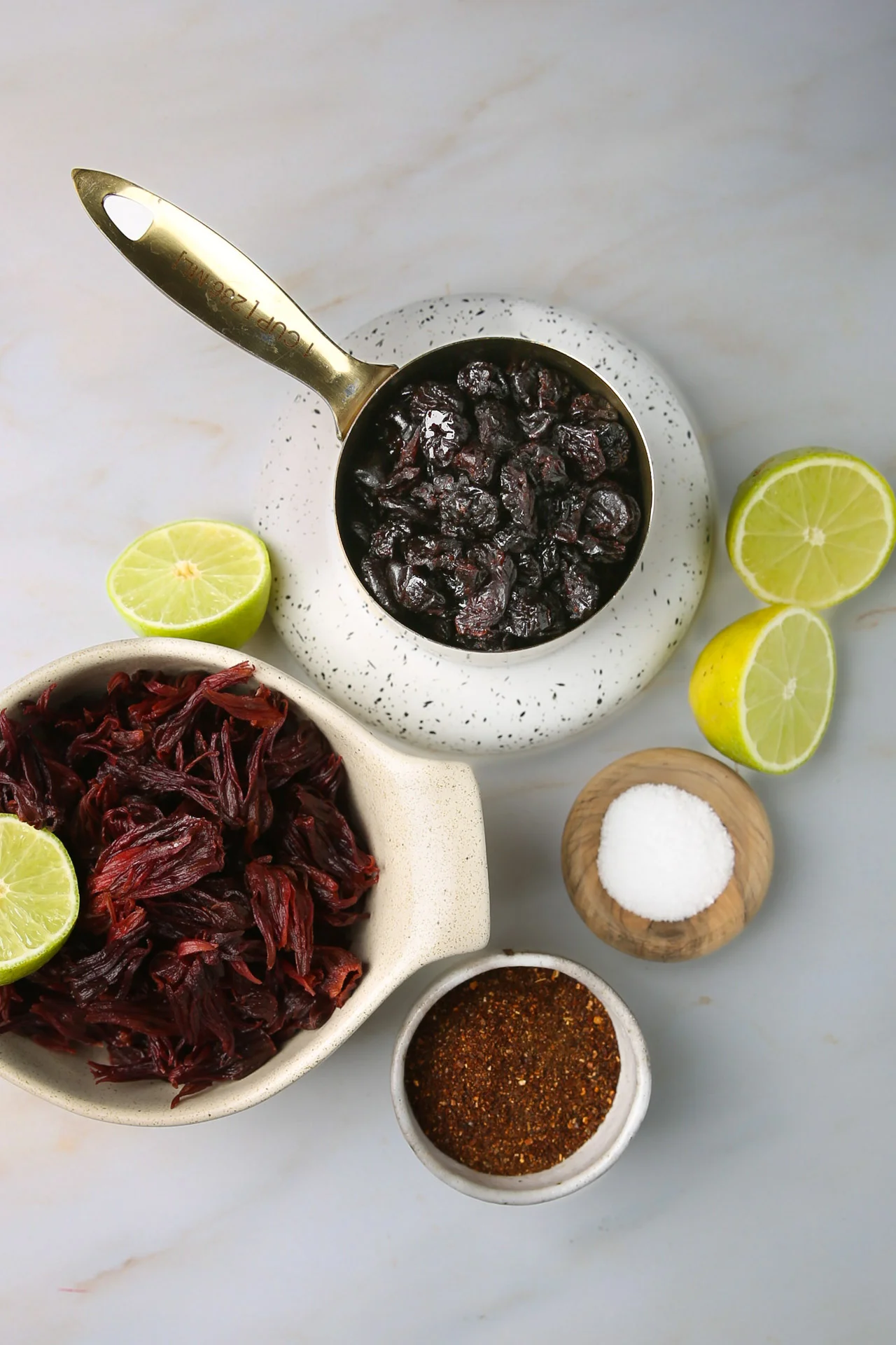 Vista de arriba de los ingredientes para chamoy de jamaica: flores de jamaica, fruta seca, chile en polvo, sal y limones partidos